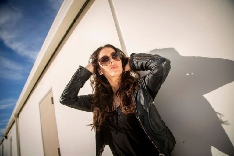 brunette woman wearing leather jacket and sun glasses standing outdoors