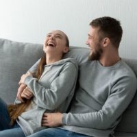 couple laughing hard inside the living room with gray sweater in a gray couch