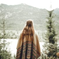 donna con poncho marrone che guarda la montagna