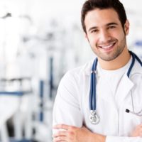 médico masculino sonriente con estetoscopio alrededor del cuello de pie dentro del gimnasio sonriendo