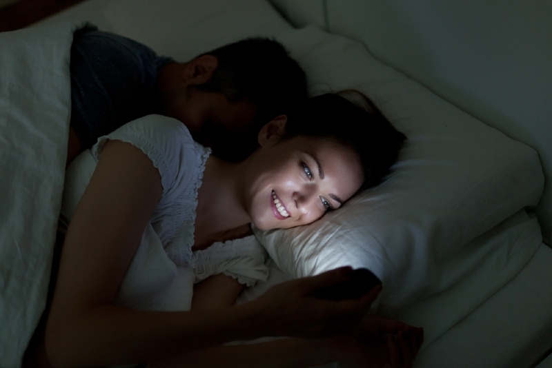 woman looking at phone while lying next to man in bed