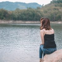 mujer con top negro sentada en una piedra cerca del agua