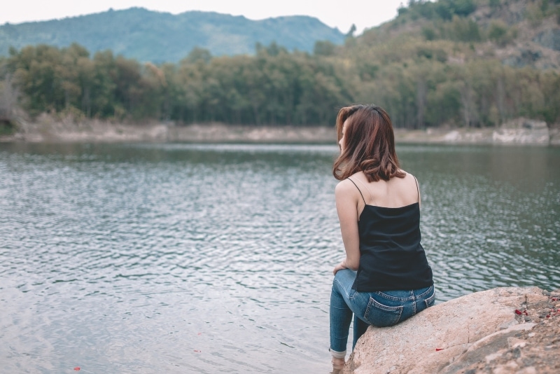 woman in black top sitting on stone near water
