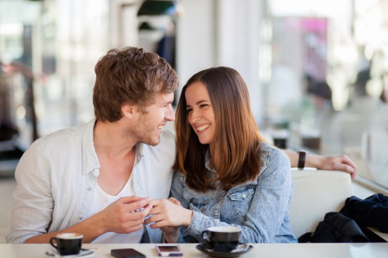 cheerful couple talking inside a cafe with their coffee