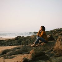 mujer con jersey amarillo sentada en una roca mirando al mar