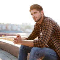 pensive guy in plaid shirt sitting by the roadside