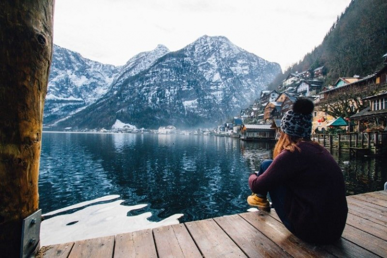 woman in purple sweater sitting on dock looking at mountain