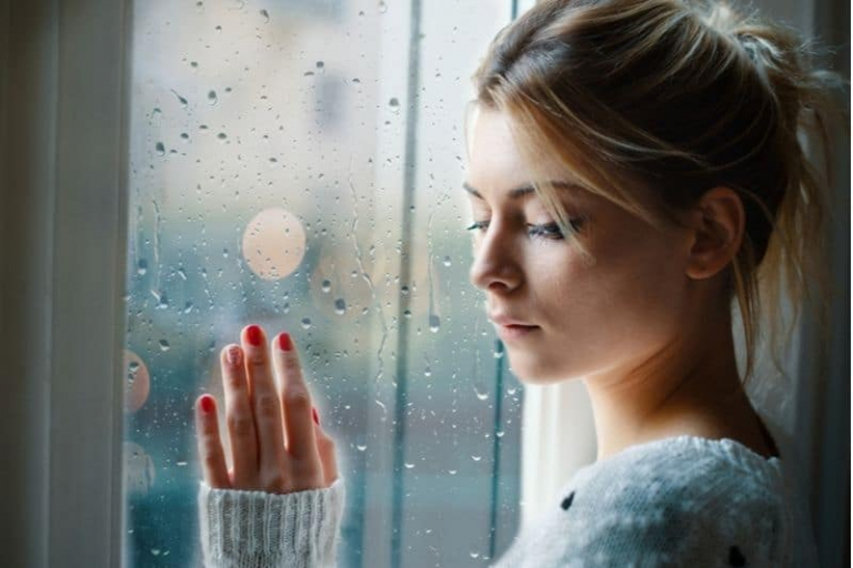 young sad girl looking out the window holding on the glass window