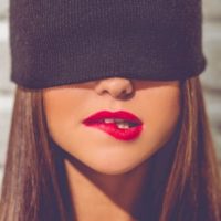 stylish young woman with black cap on hiding her eyes biting her lip
