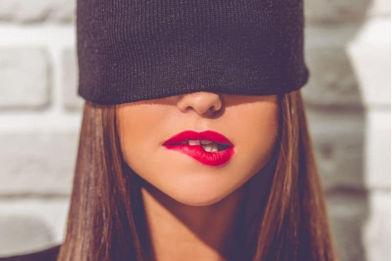 stylish young woman with black cap on hiding her eyes biting her lip