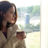 pensive woman drinking coffee near the glass windows