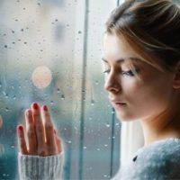 lonely and sad woman touching the glass windows with a raindrops on the glass