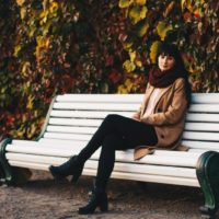 woman in brown coat sitting on white bench