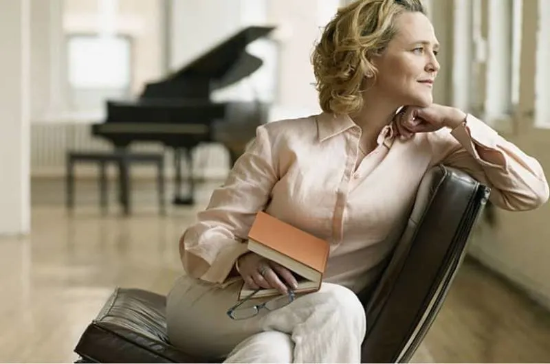 adult holding a book putting it on her lap while looking outside the window