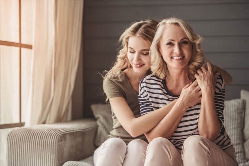 beautiful mom and daughter bonding hugging and sitting in the couch inside living room