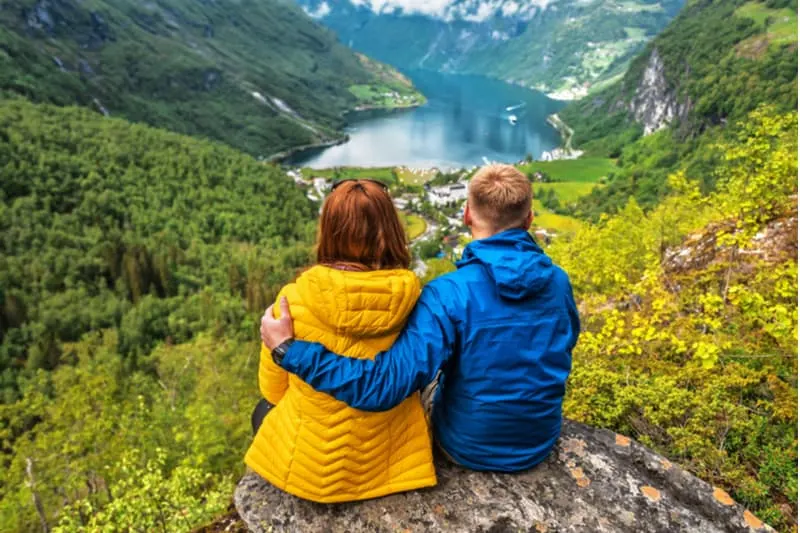 blue yellow couple sitting on a rock overlooking a body of water in the midst of the mountains