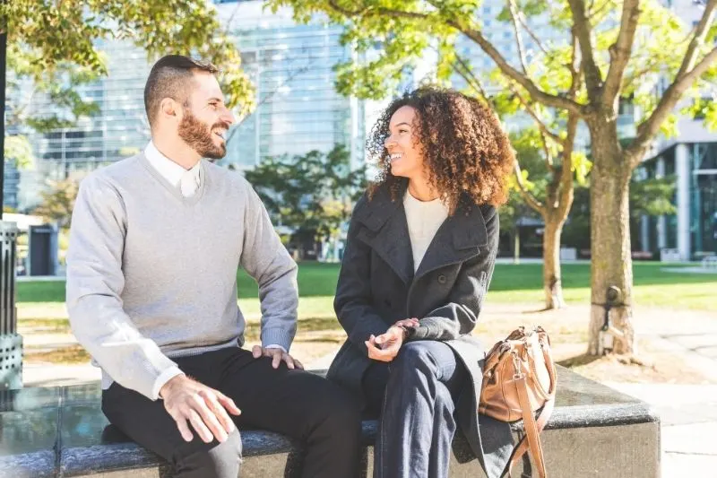 business woman and man talking and sitting in the bench outdoors
