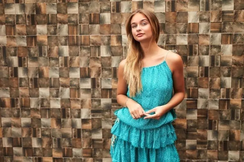 confident woman in blue green dress standing against a knitted wall