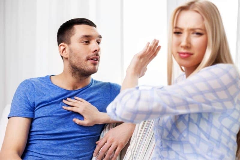 couple having a fight woman stopping man to talk whilst sitting on sofa inside living room