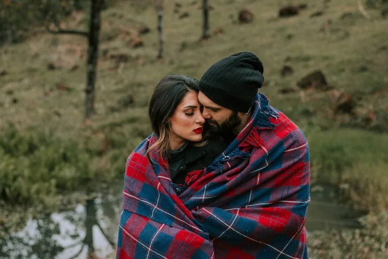 man and woman hugging covered in red and black blanket