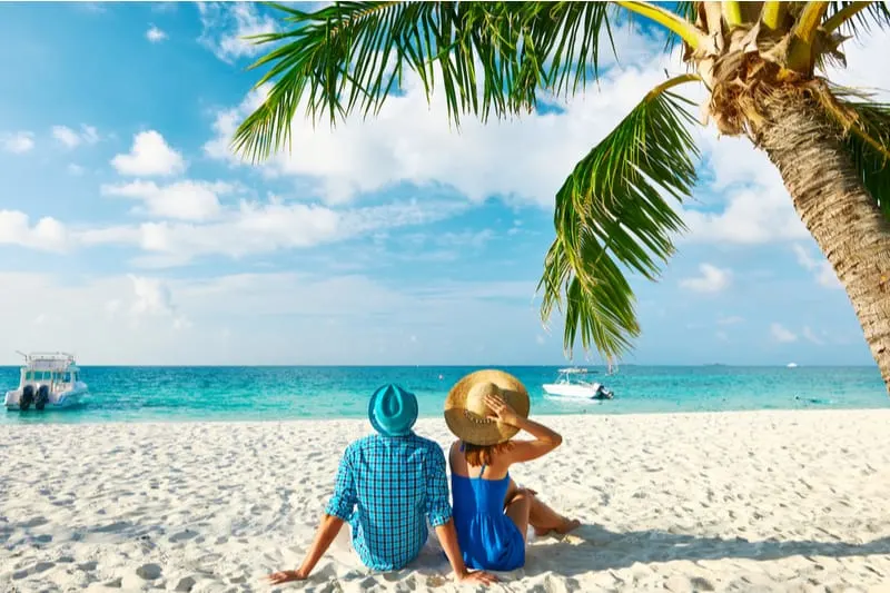couple in blue and green clothes relaxing in a tropical beach with white sand