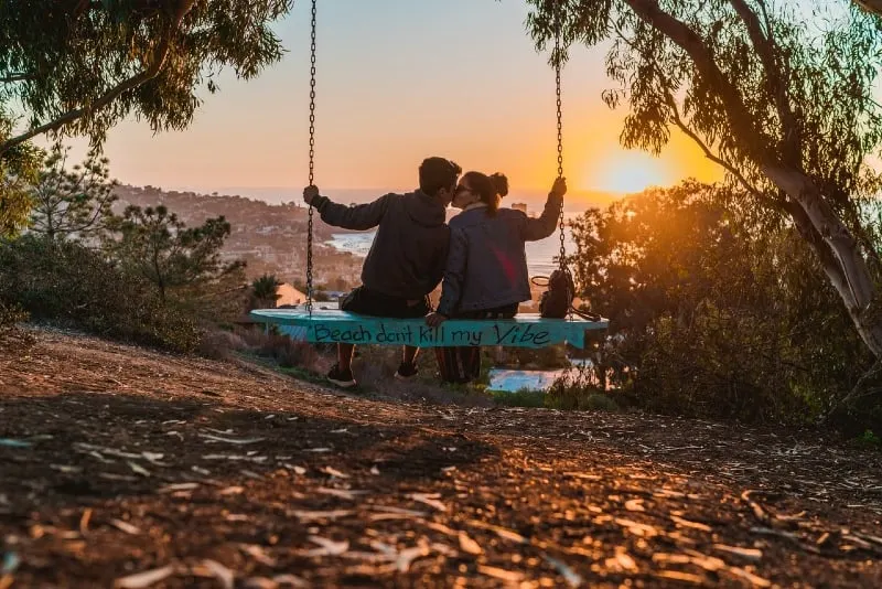 man and woman kissing while sitting on swing during sunset