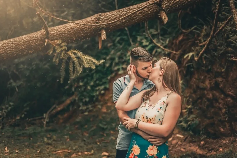 man and woman kissing near tree