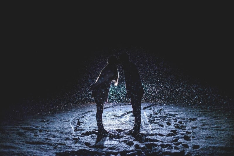 man and woman kissing on snowfield at night