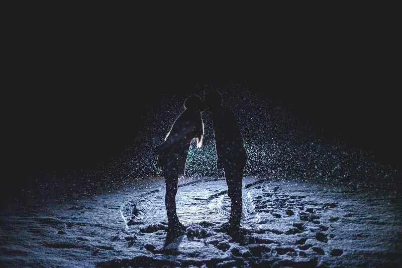 man and woman kissing on snowfield at night
