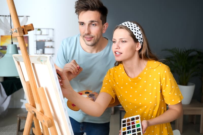 mujer con camiseta amarilla y hombre pintando interior