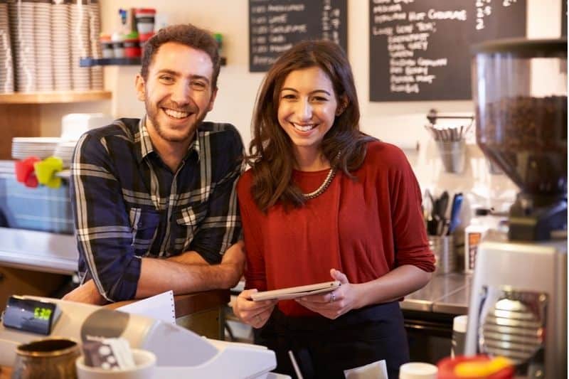 pareja que regenta una cafetería posando cerca del mostrador de caja