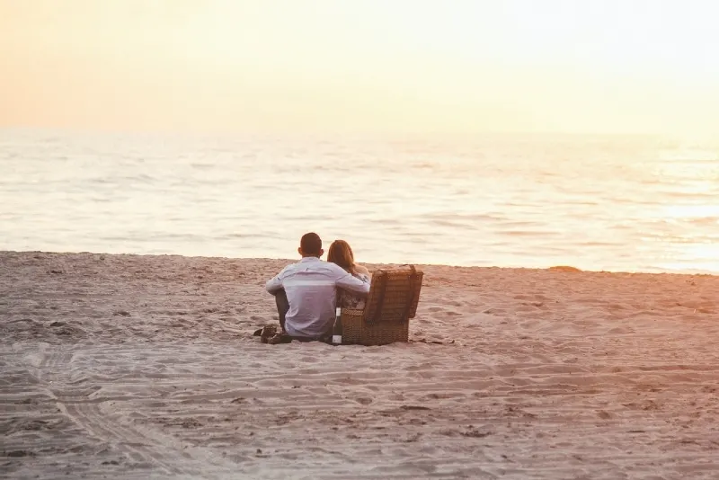 man and woman sitting on beach looking at sea