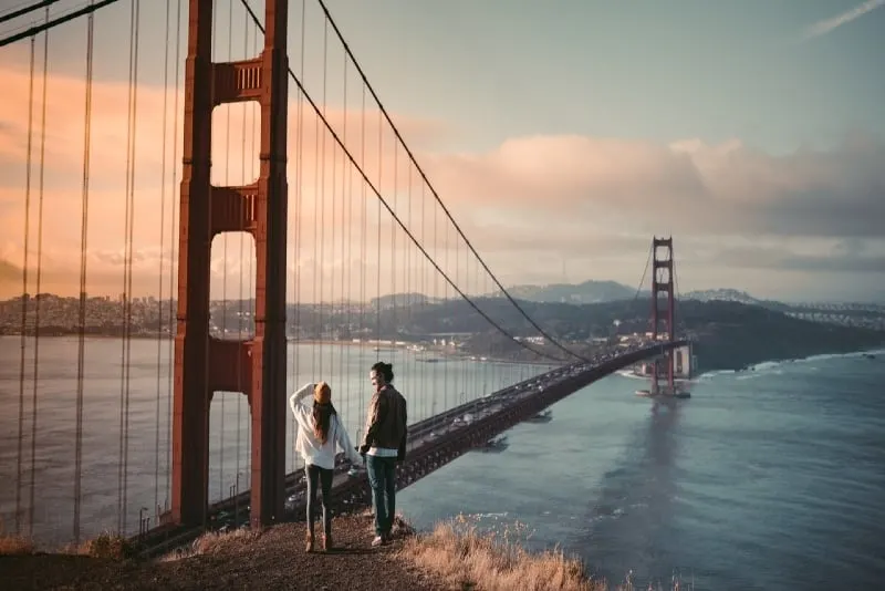 man and woman holding hands standing near golden gate bridge