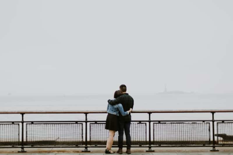 man and woman hugging while standing near fence