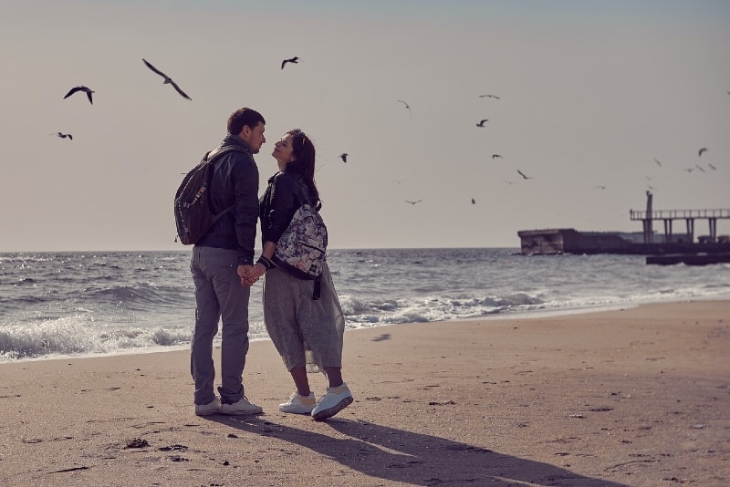 uomo e donna che si tengono per mano in piedi sulla spiaggia