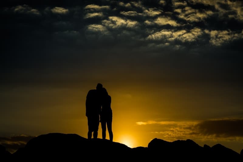 uomo e donna in piedi su una collina durante il tramonto