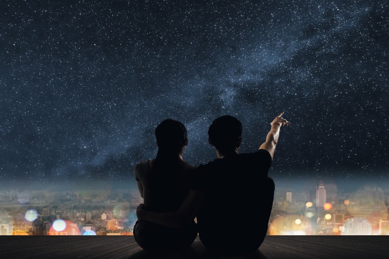 hombre y mujer mirando las estrellas sentados en un tejado