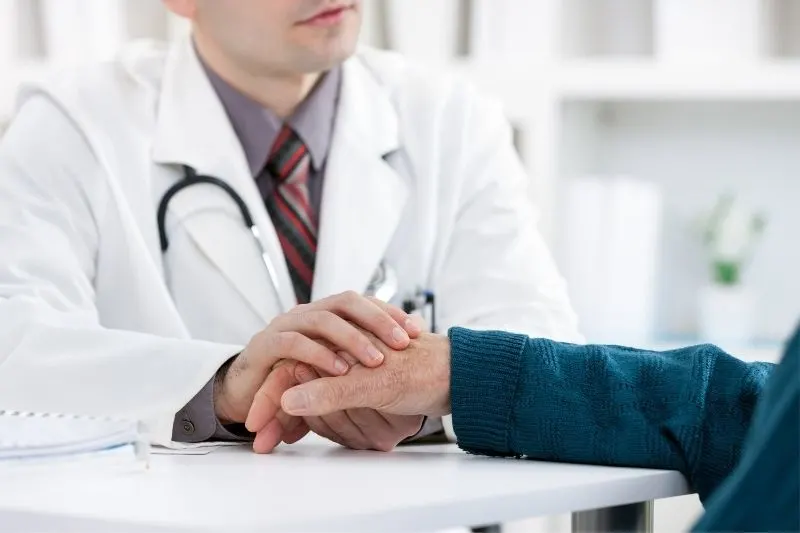 cropped image of a doctor holding hand of an old person/patient inside clinic