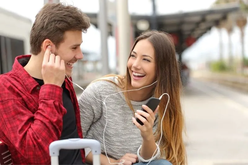 cute couple listening to music in the cellphone sitting outdoors