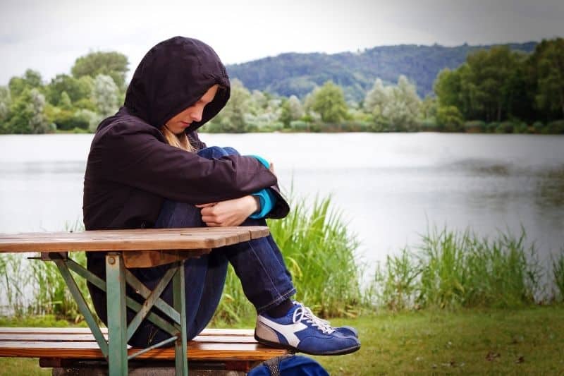 depressive and sad girl sitting on the bench near a body of water