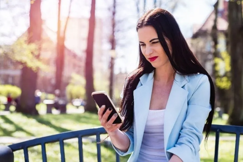 disgusted woman looking at her smartphone outdoors