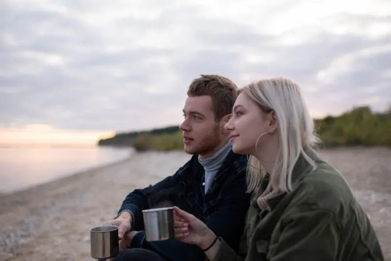 dreamy couple with tea resting in the countryside near a body of water