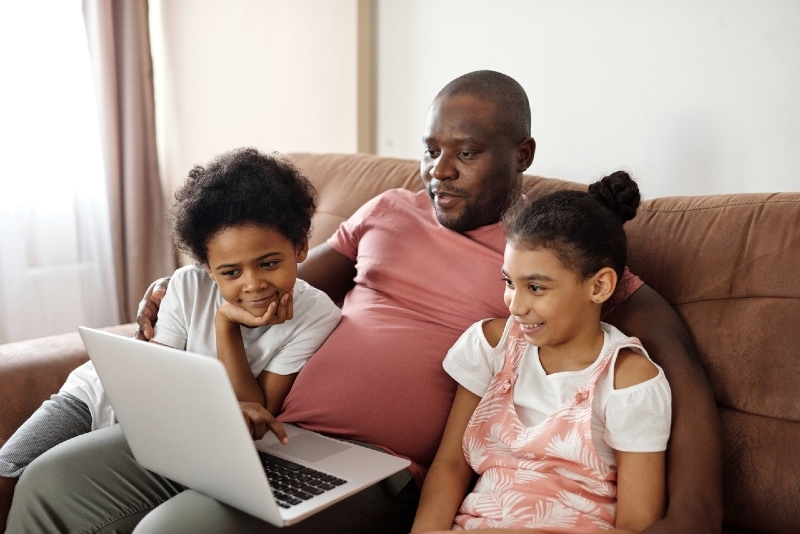 pai e filhos a olhar para o computador portátil enquanto estão sentados no sofá