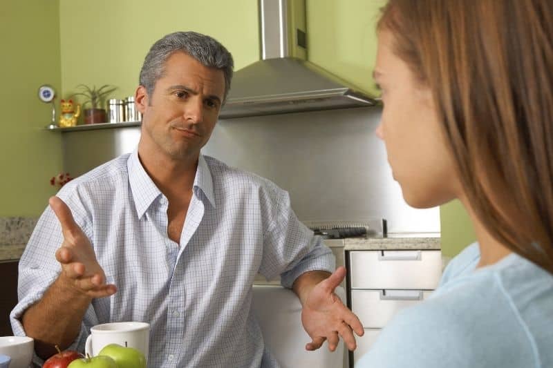 father talking to daughter inside kitchen while sitting by the table 