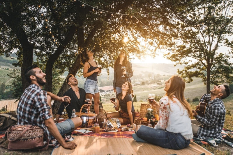 group of friends having picnic near trees