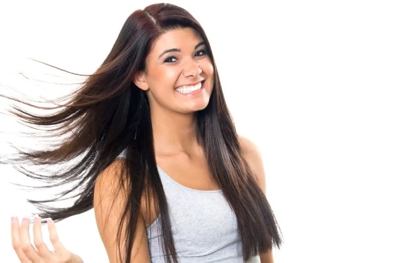 good hair day of a woman smiling flipping her hair standing against a white wall