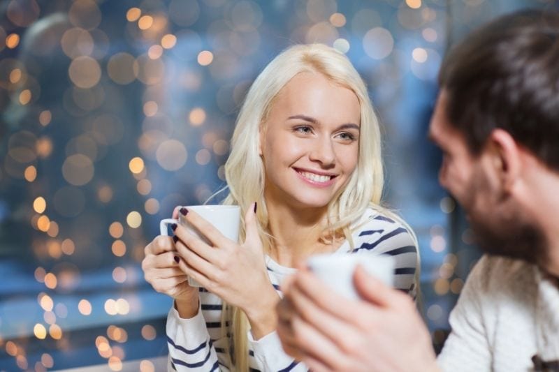 coppia felice che si incontra in un caffè tenendo una tazza con le luci di serie fuori il caffè