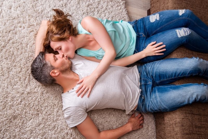 pareja besándose tumbados en la alfombra con los pies en el sofá dentro del salón