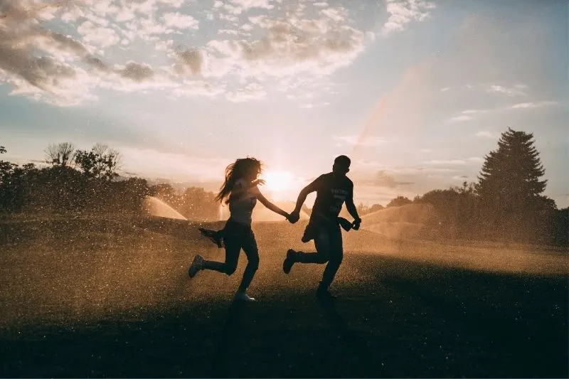 lovers runnung in rain spray during sunset in silhouette