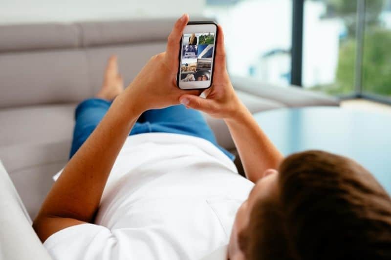 man browsing social media lying down on sofa inside living room